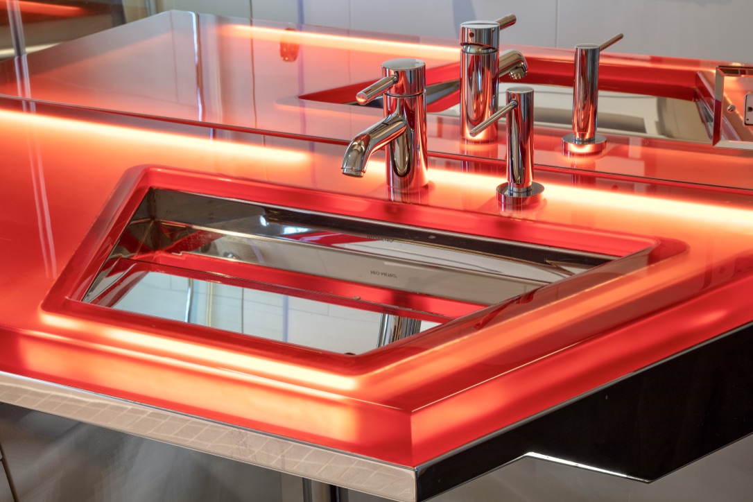 A red sink with two faucets and a mirror.