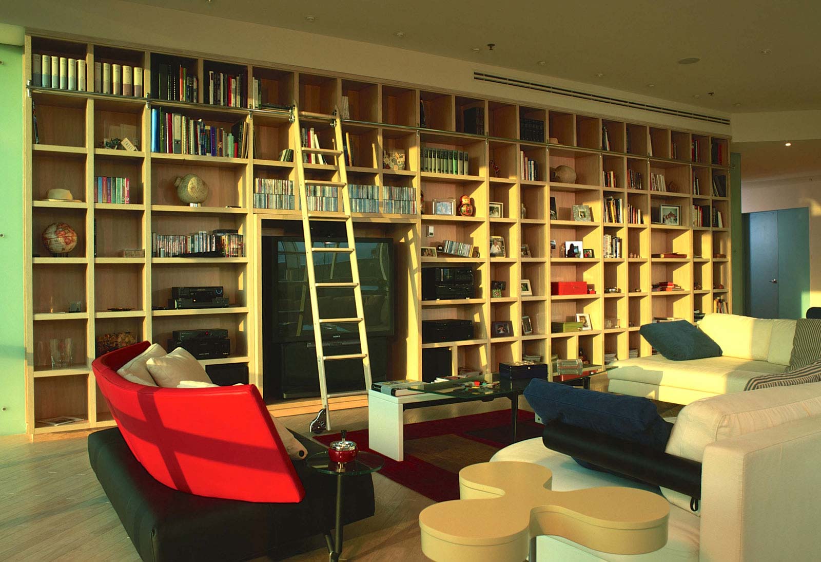 A living room with a large book case and ladder.